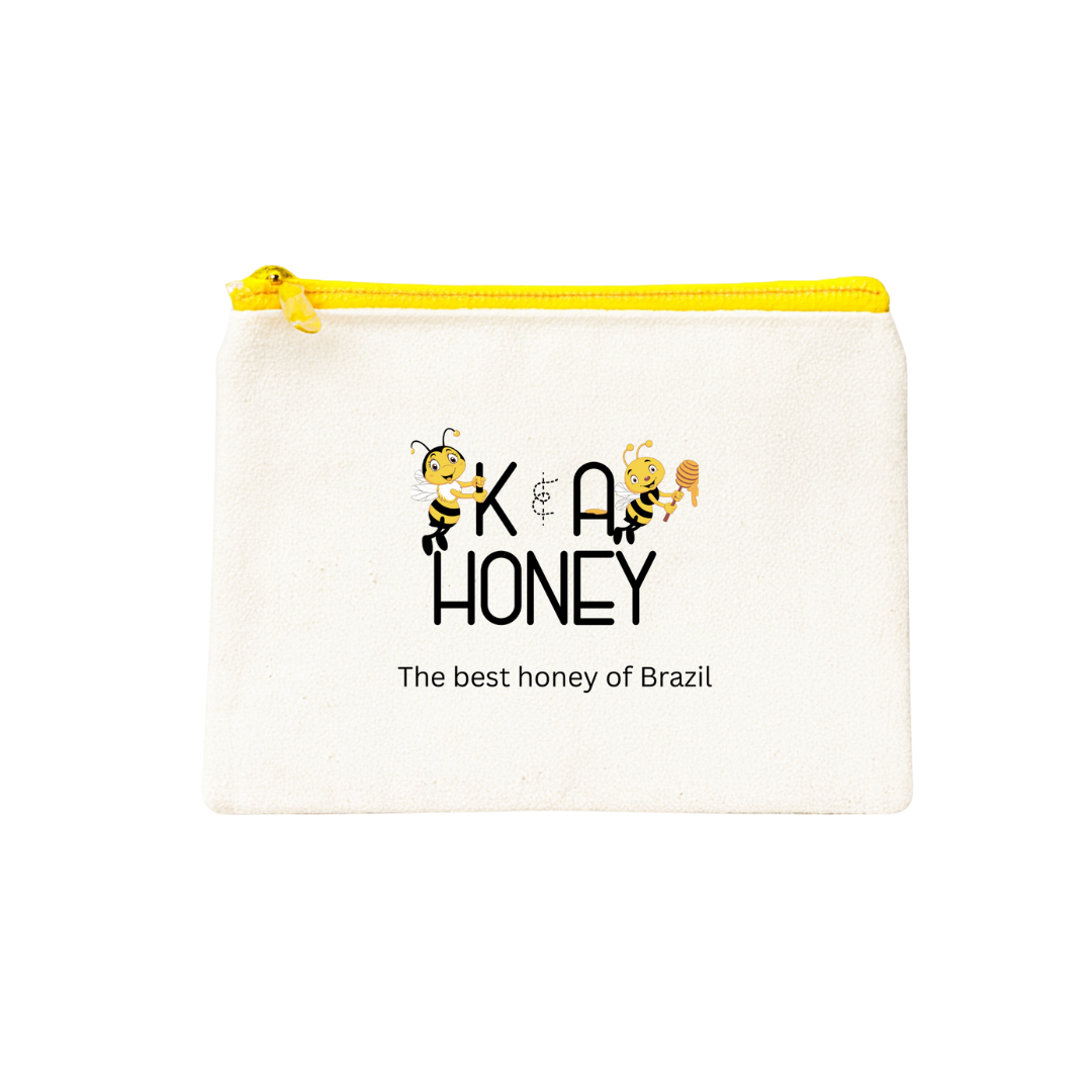 White zippered pouch featuring two cartoon bees holding letters 'K' and 'A' with a honey dipper, stylized 'K & A HONEY' text, and tagline 'The best honey of Brazil'.