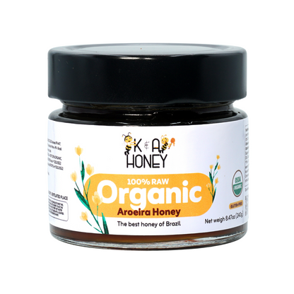 "Jar of K&A Honey labeled '100% RAW Organic Aroeira Honey' with USDA Organic certification, black lid, and white label featuring yellow and green floral graphics; golden honey inside, net weight 8.4oz (240g), emphasizing Brazilian origin and organic quality.