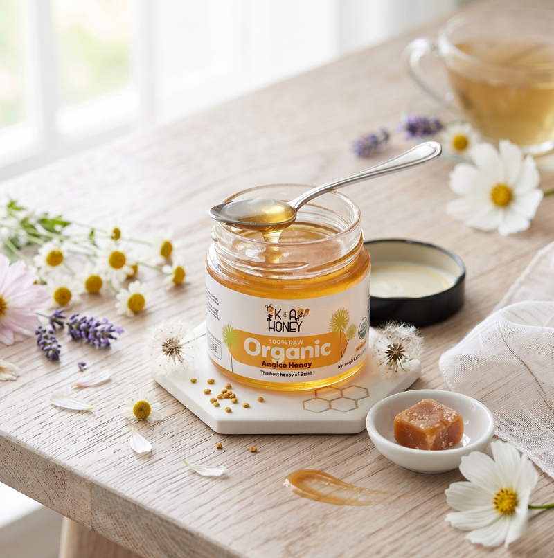 Jar of organic honey with a spoon on a wooden table with flowers and tea.