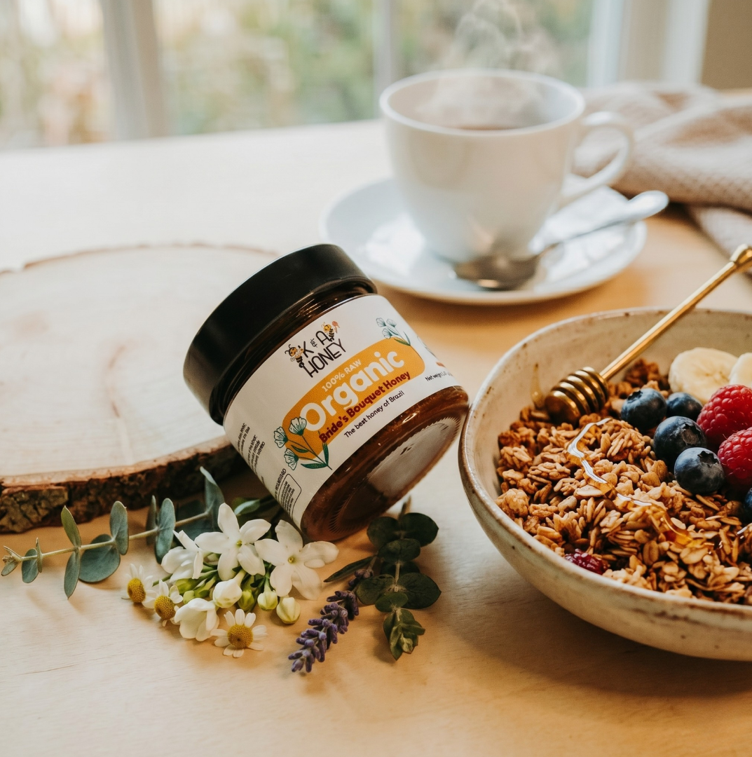 Jar of Nutella, bowl of granola with berries, and cup of coffee on a wooden table.